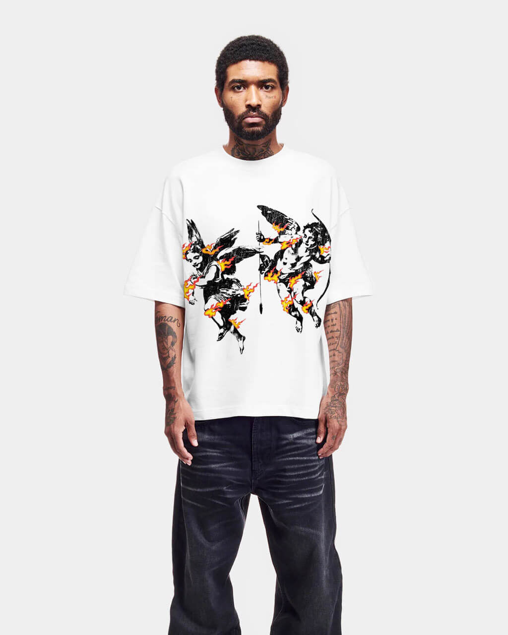 Man wearing a white t-shirt with black and orange angels on fire design and dark jeans on a white background