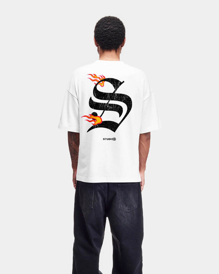 Man wearing a white t-shirt with black and orange angels on fire design and dark jeans on a white background