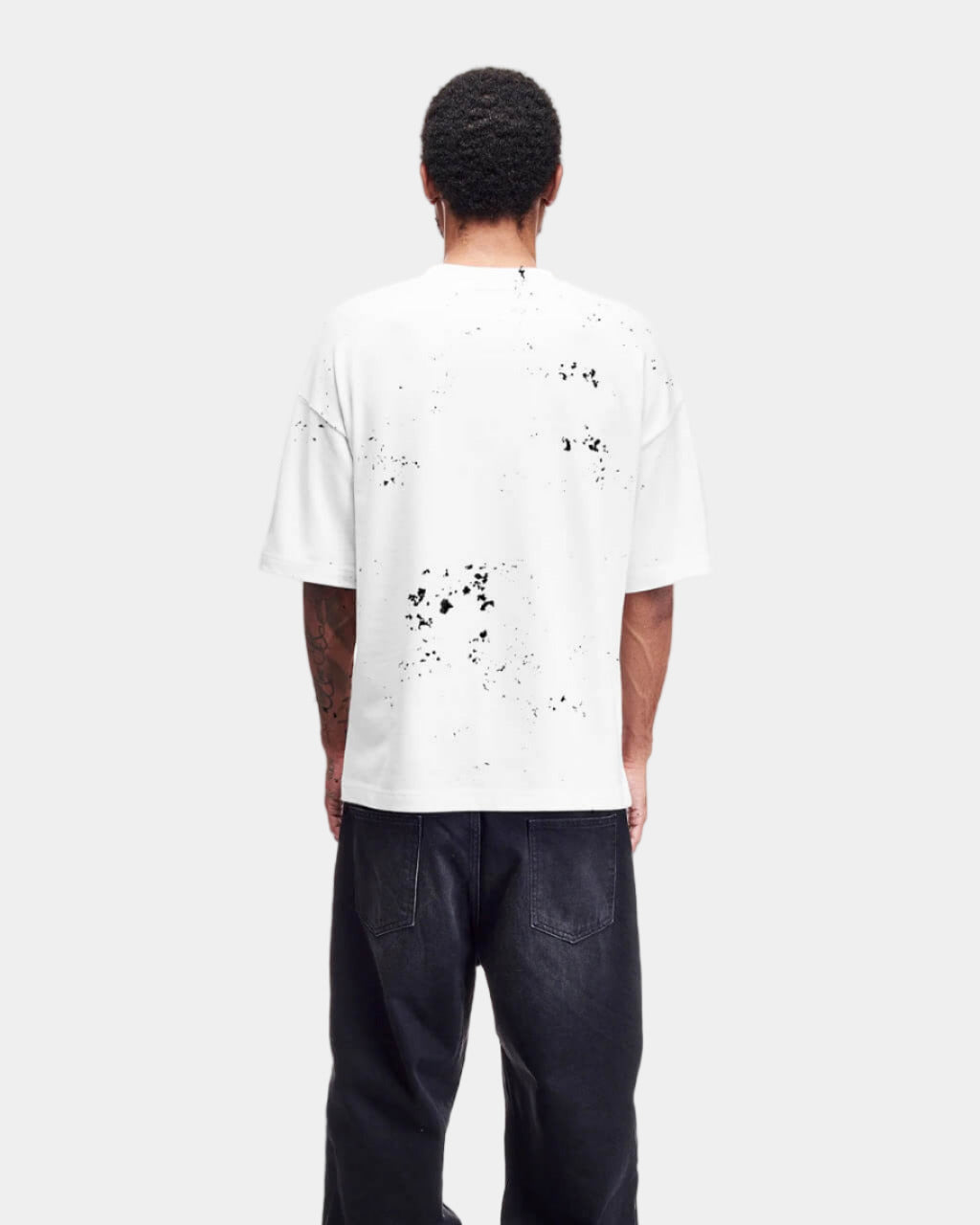 Person wearing a white t-shirt with black splatter design and black pants on a white background