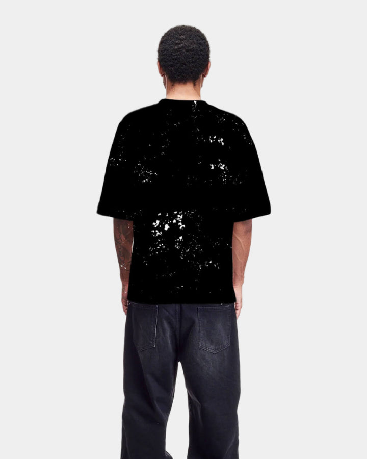 Person wearing a black t-shirt with white splatter design and black pants on a white background