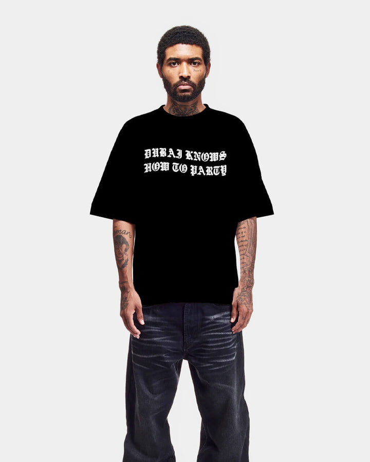 Person wearing a black t-shirt with text and dark pants on a white background