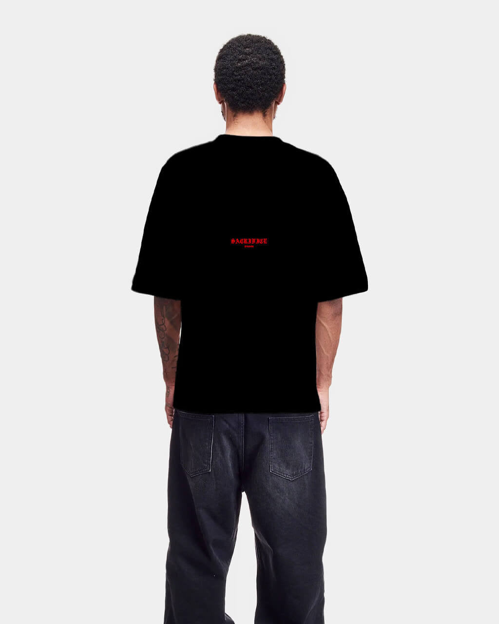 Person wearing a black t-shirt with red text on the back, standing against a white background
